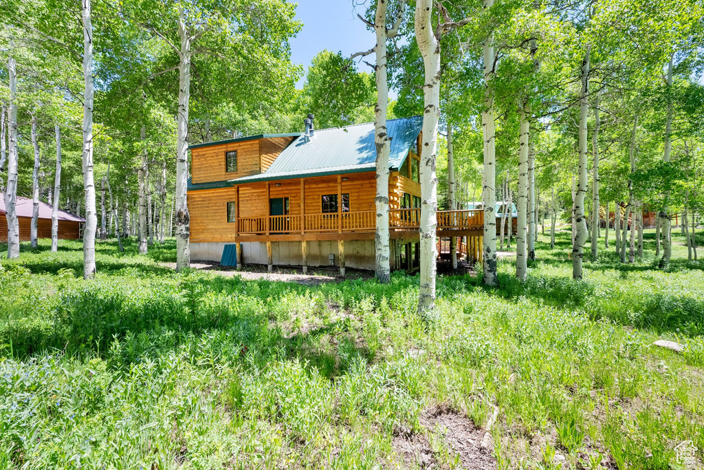 Back of property with a wooden deck, metal roof, and view of wooded area