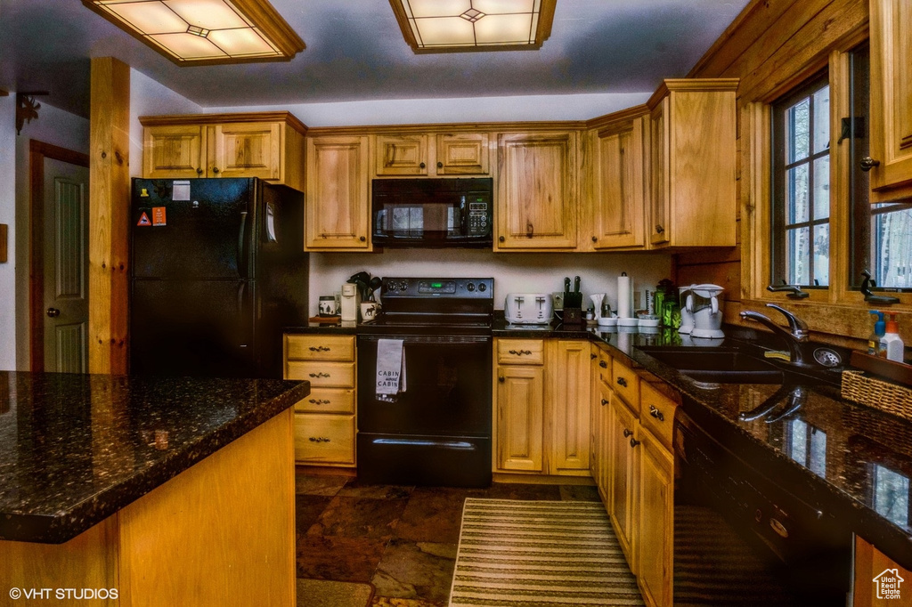 Kitchen with brown cabinetry, a sink, dark stone countertops, and black appliances