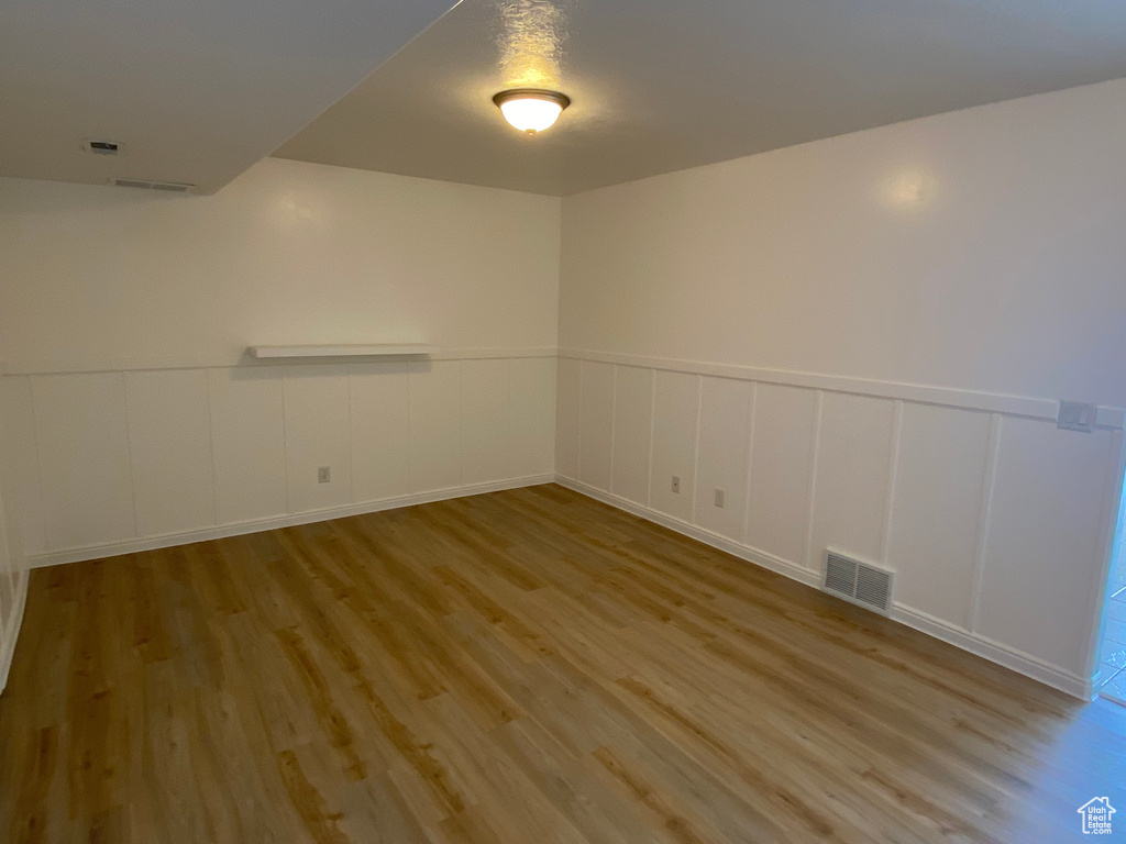 Empty room featuring a decorative wall, wainscoting, wood finished floors, and visible vents