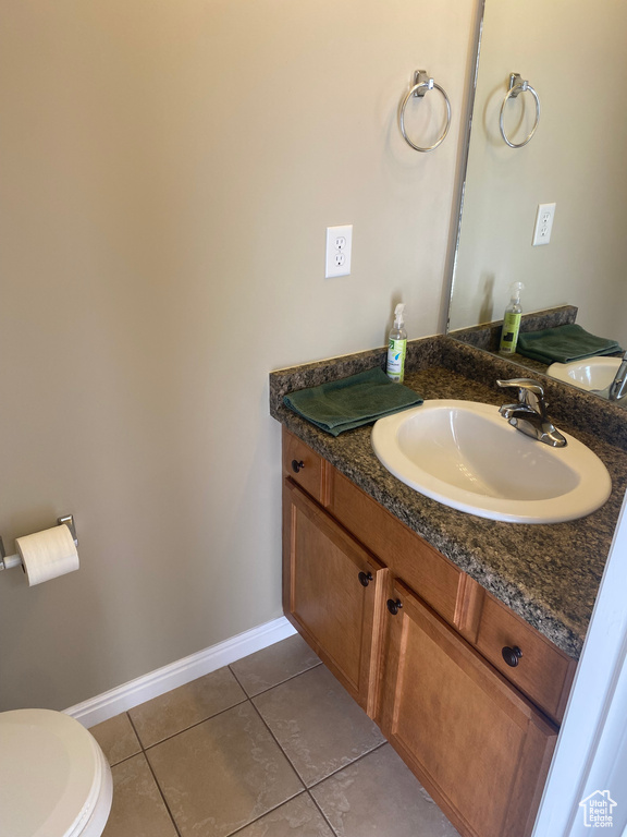 Half bathroom featuring vanity, baseboards, tile patterned floors, and toilet