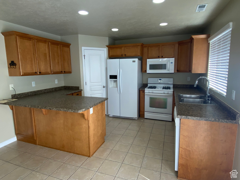 Kitchen with dark countertops, a sink, a peninsula, recessed lighting, and white appliances