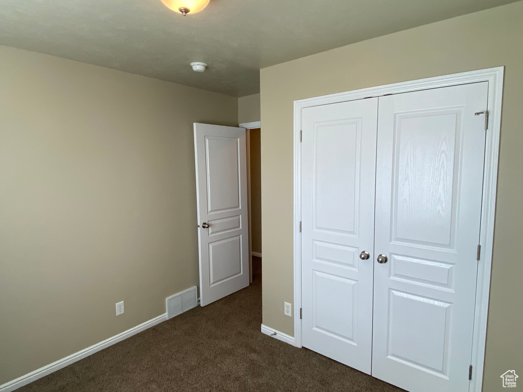 Unfurnished bedroom featuring visible vents, baseboards, dark carpet, and a closet