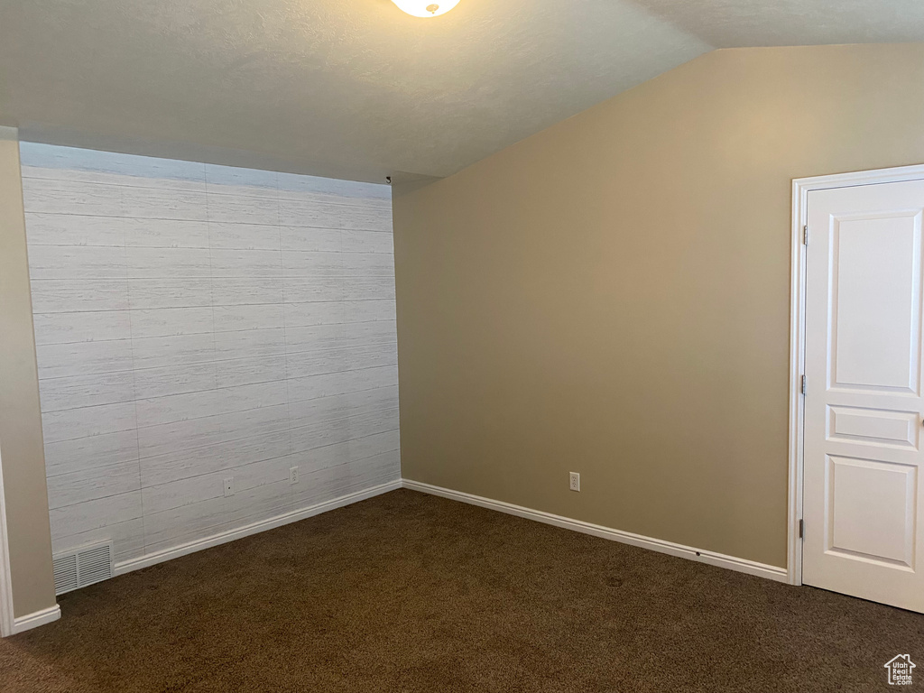 Unfurnished room featuring baseboards, vaulted ceiling, dark carpet, and visible vents