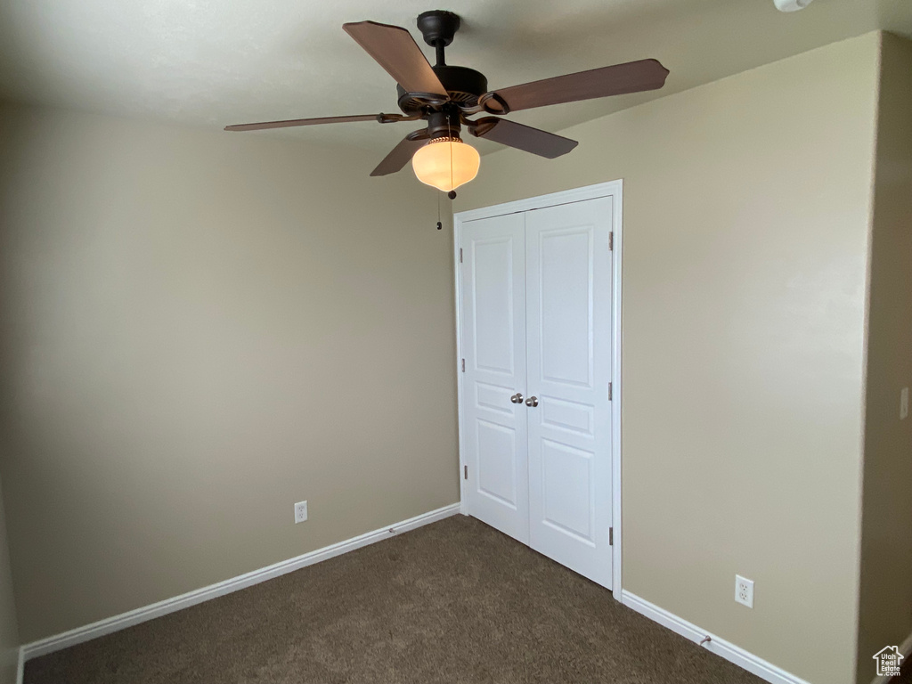 Unfurnished bedroom with dark carpet, baseboards, ceiling fan, and a closet
