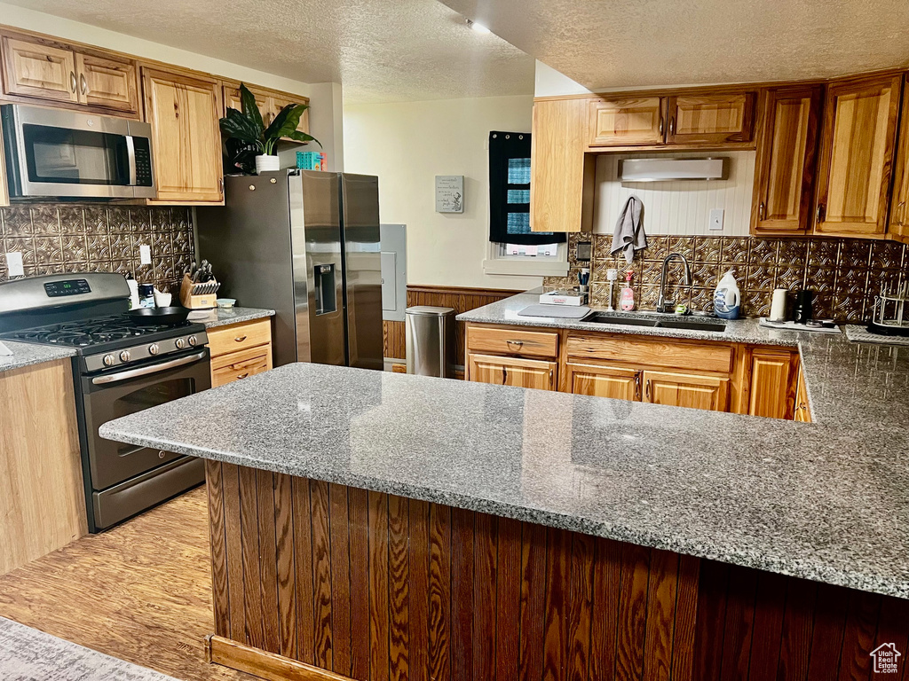 Kitchen with light stone counters, a sink, a textured ceiling, stainless steel appliances, and tasteful backsplash