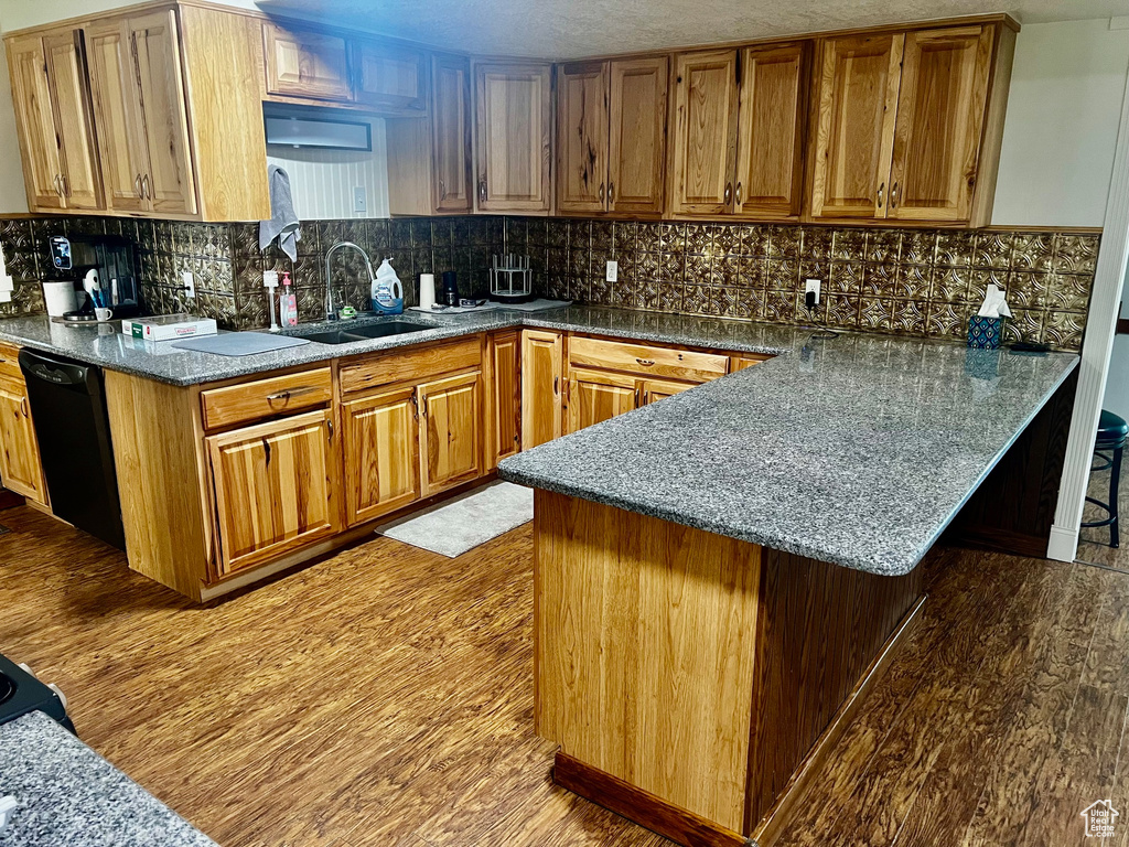 Kitchen featuring a sink, dishwasher, a peninsula, wood finished floors, and backsplash