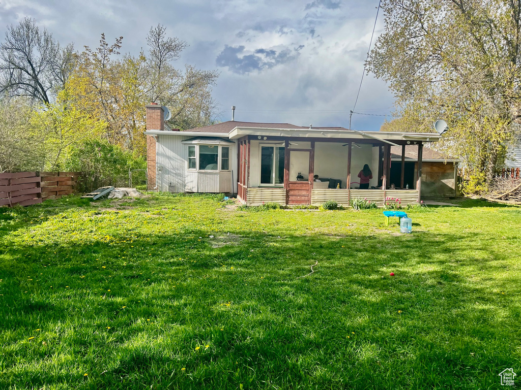 Back of property featuring fence, a lawn, a chimney, and a sunroom