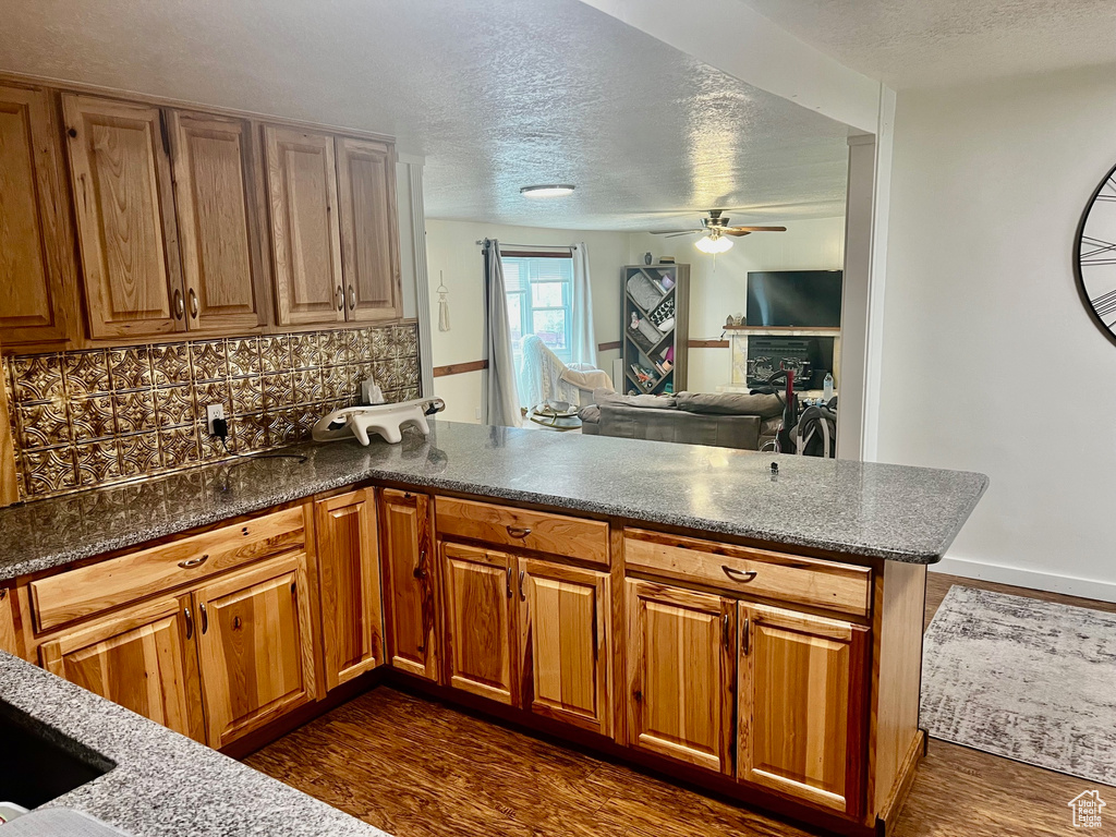 Kitchen featuring dark wood-style flooring, a ceiling fan, a peninsula, and a textured ceiling