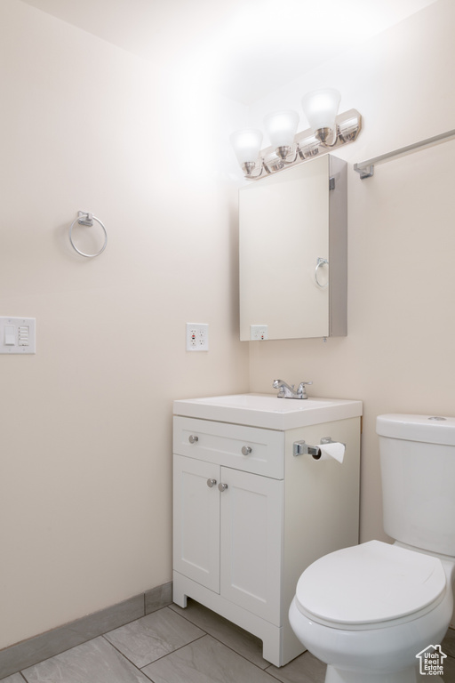 Half bath with vanity, baseboards, tile patterned floors, and toilet