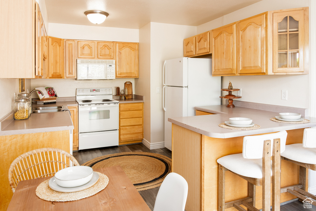 Kitchen featuring a kitchen bar, light brown cabinetry, a sink, a peninsula, and white appliances