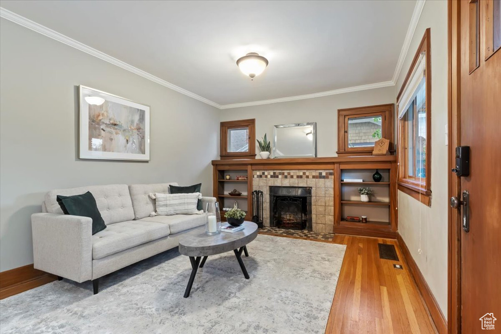 Living area featuring visible vents, ornamental molding, a fireplace, baseboards, and light wood-style flooring