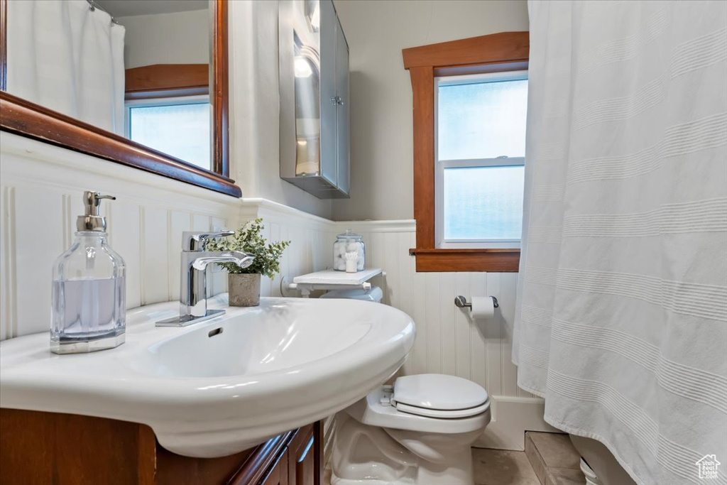 Full bath with a shower with curtain, wainscoting, toilet, and a decorative wall