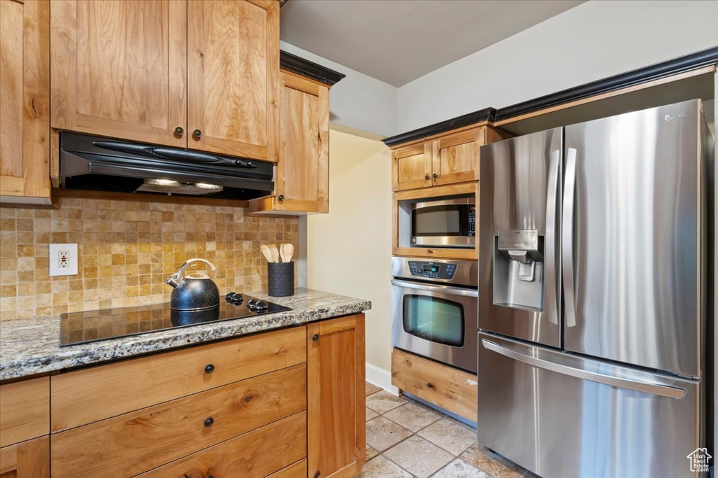 Kitchen with light stone counters, tasteful backsplash, stainless steel appliances, and under cabinet range hood