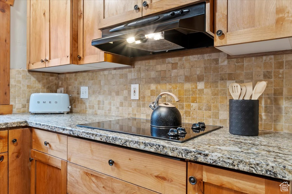 Kitchen featuring decorative backsplash, under cabinet range hood, black electric stovetop, and light stone countertops