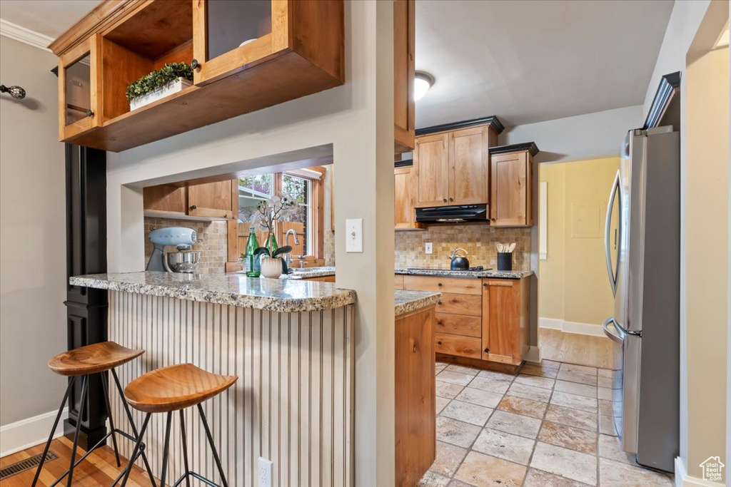 Kitchen with exhaust hood, freestanding refrigerator, a peninsula, baseboards, and tasteful backsplash