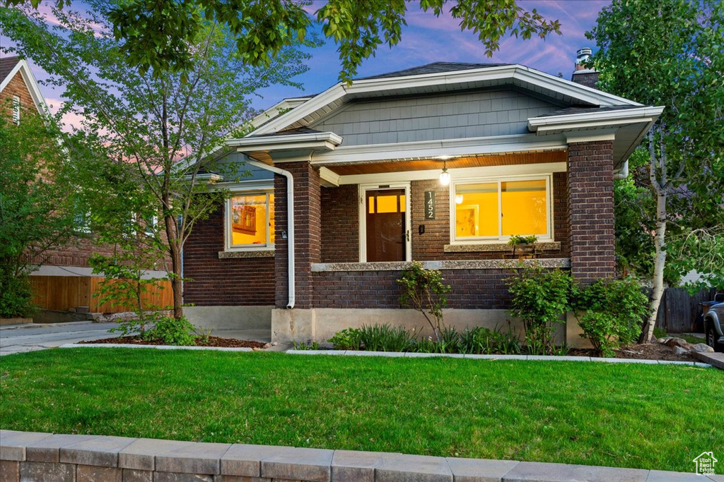 Bungalow-style house featuring covered porch, a chimney, a lawn, brick siding, and fence
