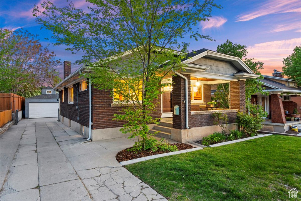 Bungalow-style home featuring a chimney, brick siding, a lawn, an outbuilding, and a detached garage