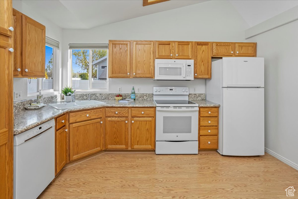 Kitchen featuring white appliances, brown cabinets, a sink, light wood finished floors, and vaulted ceiling