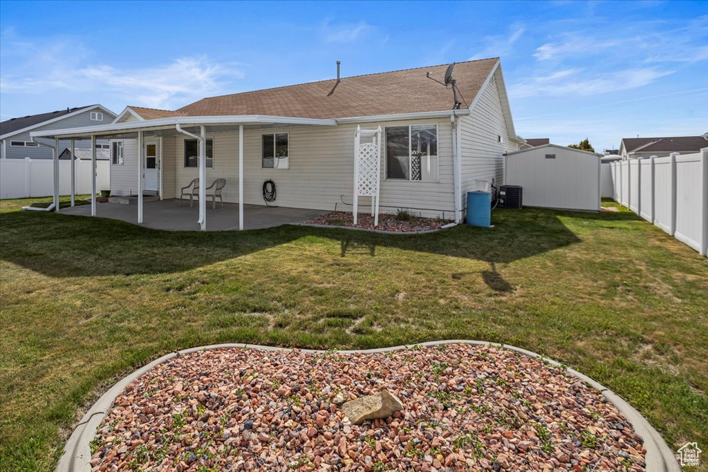 Rear view of property featuring central air condition unit, an outdoor structure, a fenced backyard, a yard, and a patio