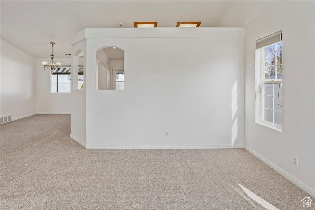 Carpeted empty room with an inviting chandelier, baseboards, and visible vents