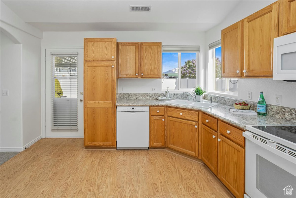 Kitchen featuring white appliances, plenty of natural light, a sink, and light wood-style flooring