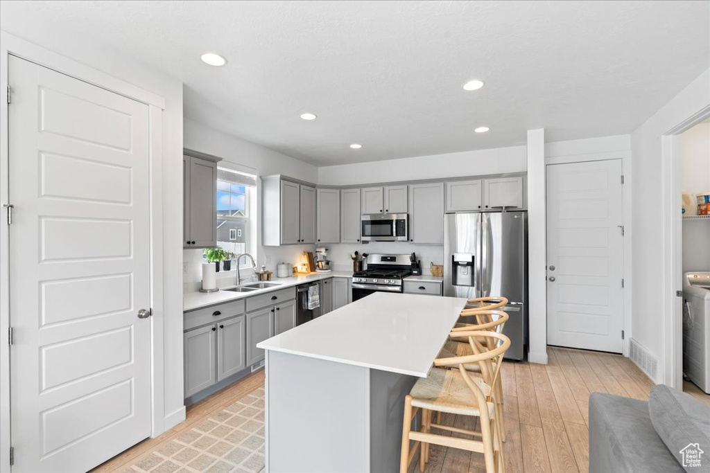 Kitchen featuring recessed lighting, appliances with stainless steel finishes, a kitchen bar, a sink, and gray cabinetry