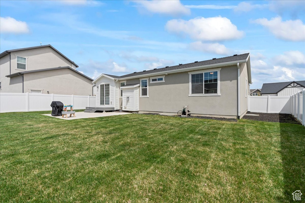 Rear view of house featuring a lawn, stucco siding, a patio, and a fenced backyard
