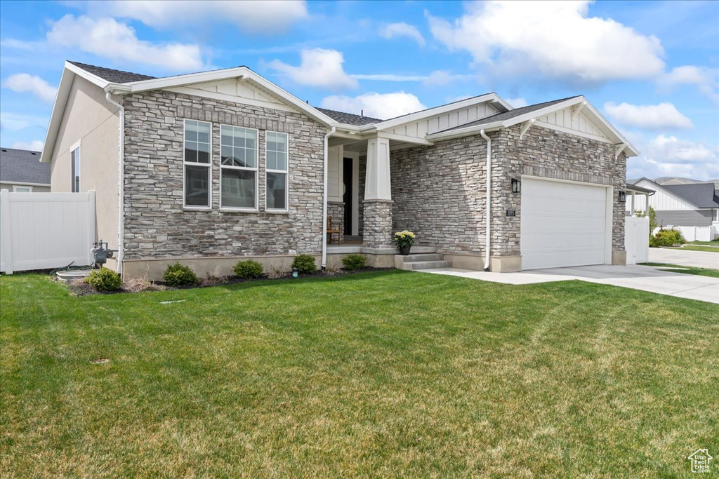 Single story home featuring fence, a garage, driveway, stone siding, and a front lawn