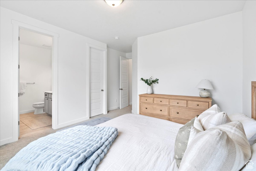 Bedroom featuring light colored carpet, ensuite bath, and baseboards