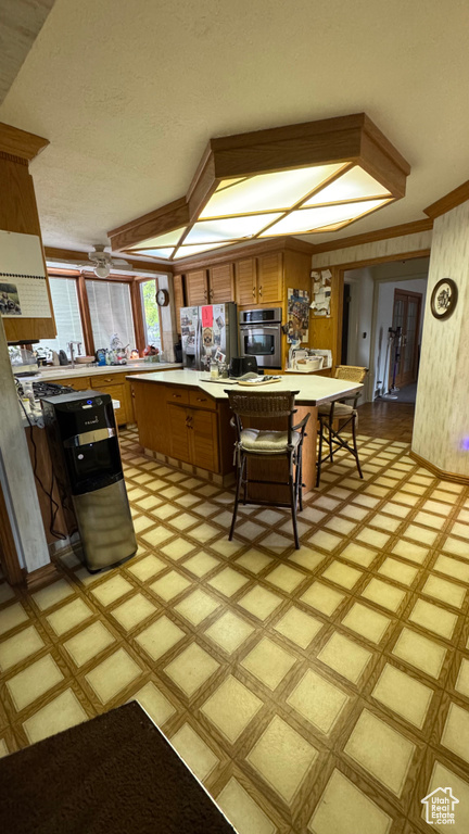 Kitchen with brown cabinetry, refrigerator with ice dispenser, light floors, and stainless steel oven