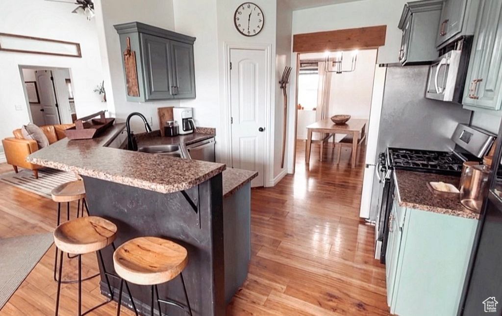 Kitchen featuring a kitchen bar, a sink, a peninsula, light wood-style floors, and stainless steel appliances