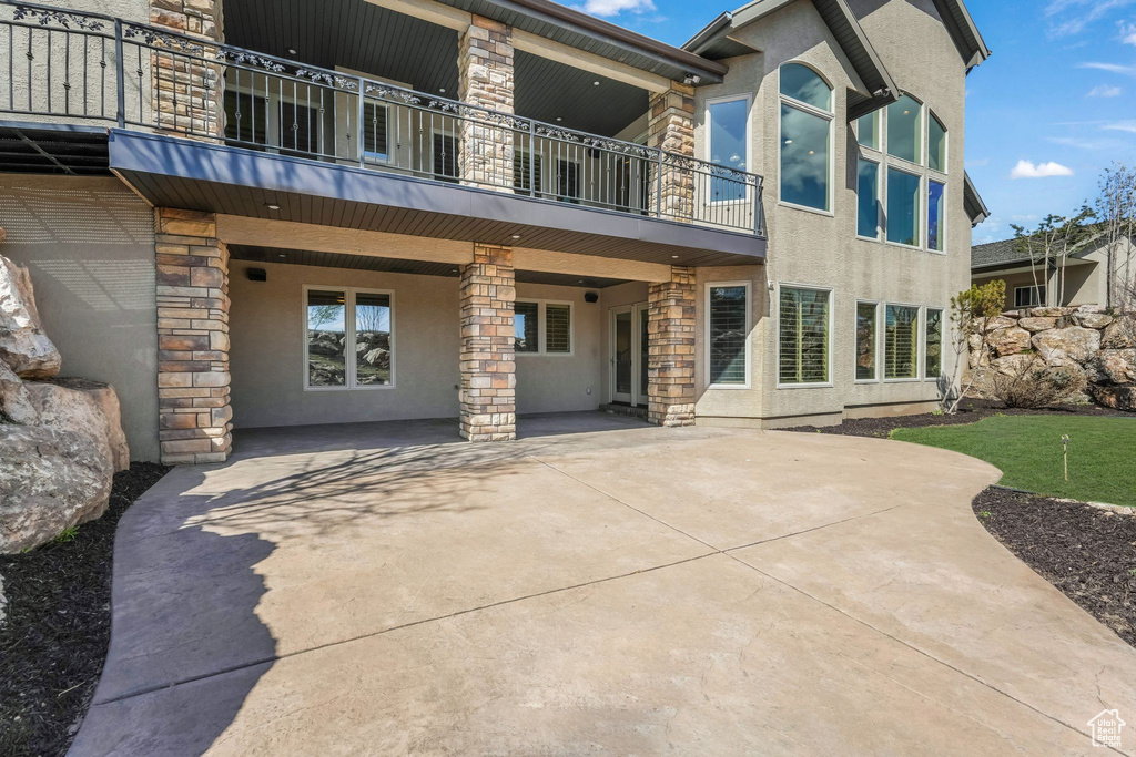 Back of house with stucco siding, a patio area, stone siding, and a balcony