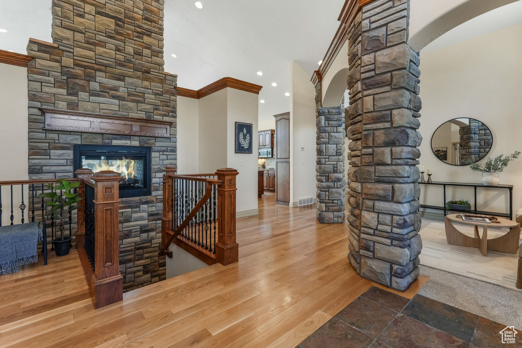 Interior space with crown molding, arched walkways, a stone fireplace, recessed lighting, and ornate columns