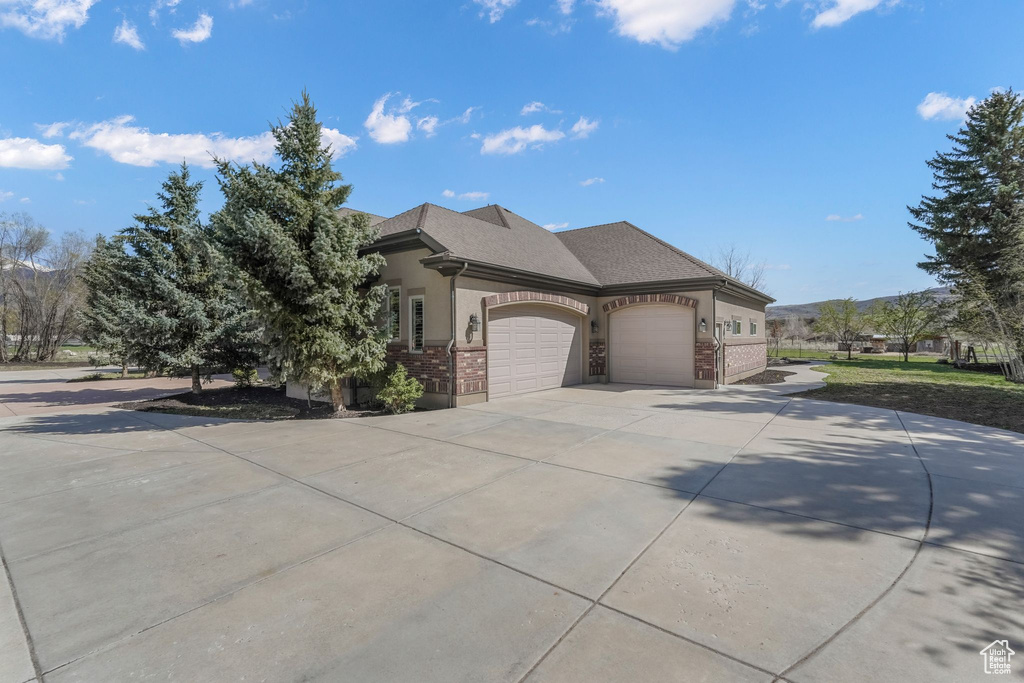 View of front of house featuring driveway, brick siding, an attached garage, a shingled roof, and stucco siding