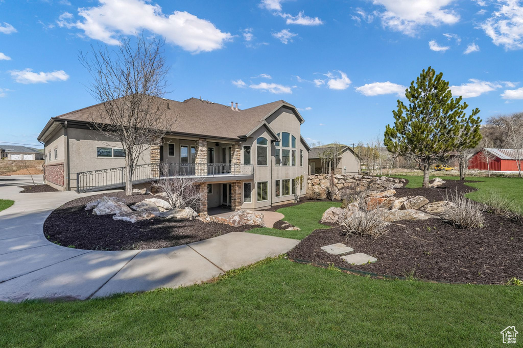 Rear view of property featuring a lawn, roof with shingles, stucco siding, and stone siding