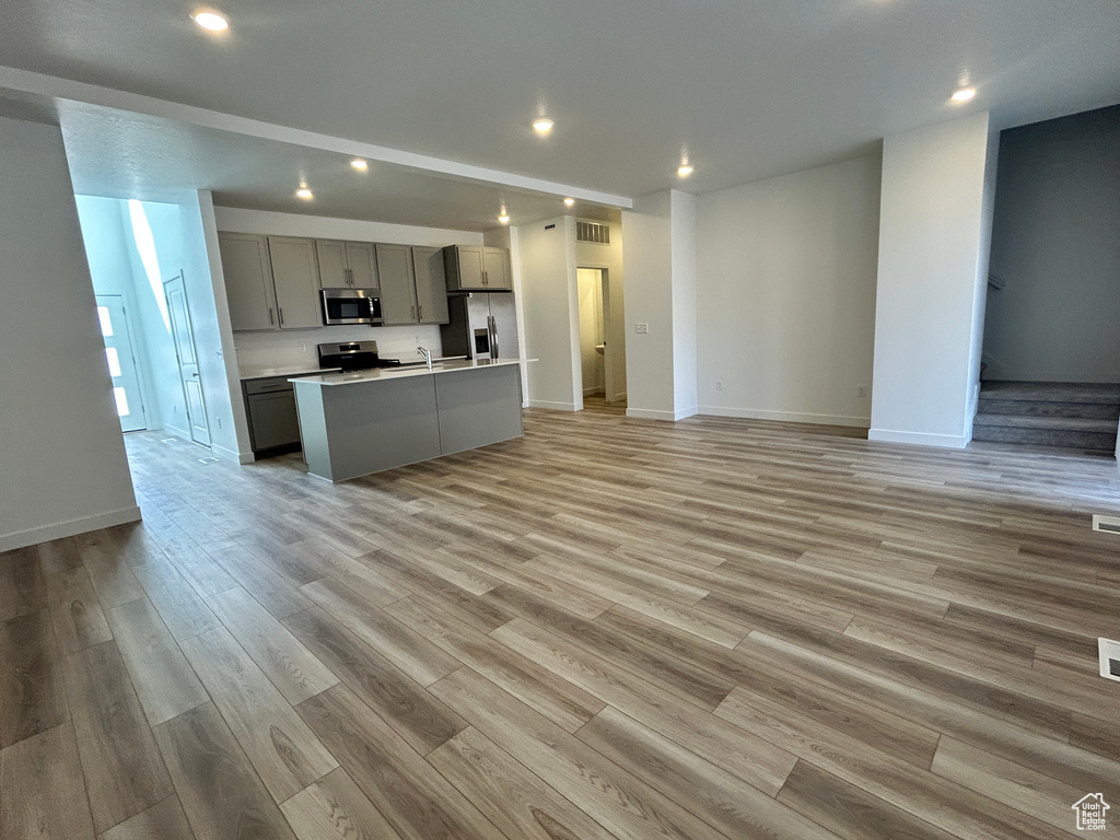 Kitchen featuring a center island with sink, gray cabinetry, open floor plan, stainless steel appliances, and recessed lighting