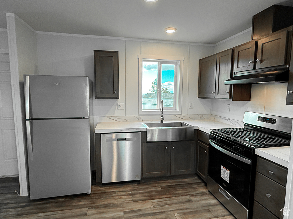 Kitchen with a sink, stainless steel appliances, under cabinet range hood, crown molding, and dark wood finished floors