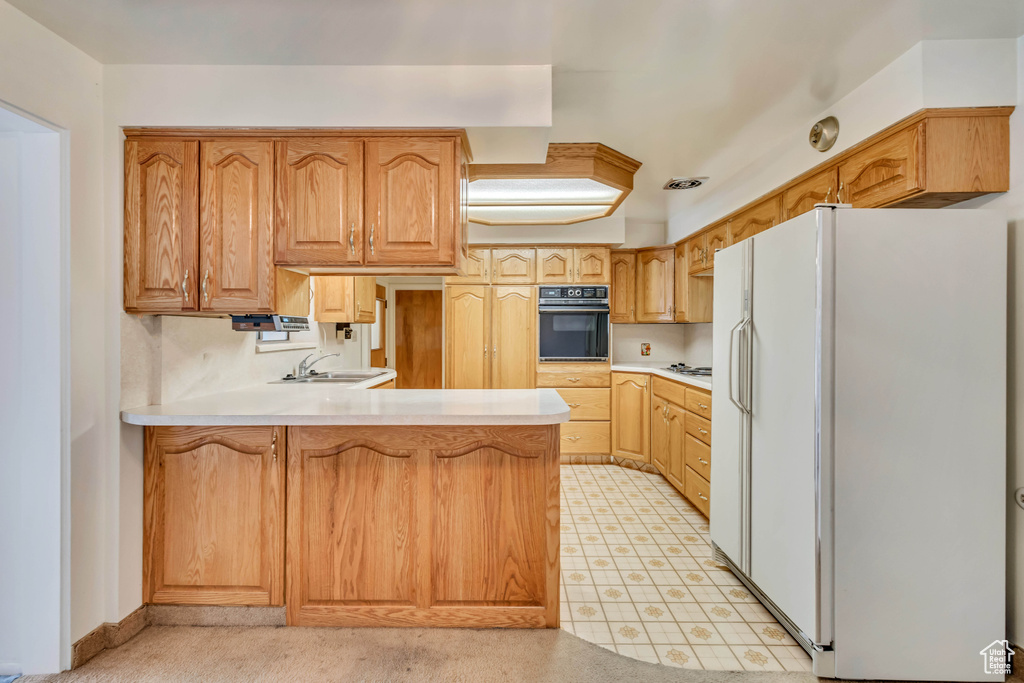 Kitchen with a sink, a peninsula, white appliances, and light countertops