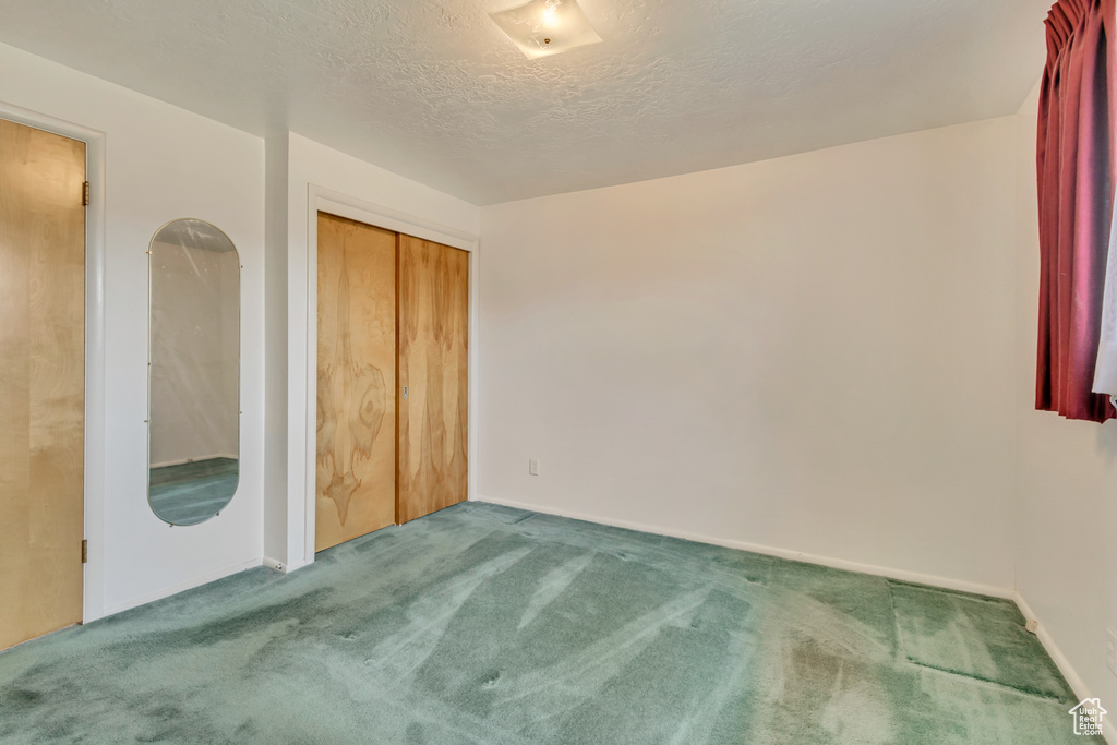 Unfurnished bedroom with baseboards, a textured ceiling, carpet, and a closet