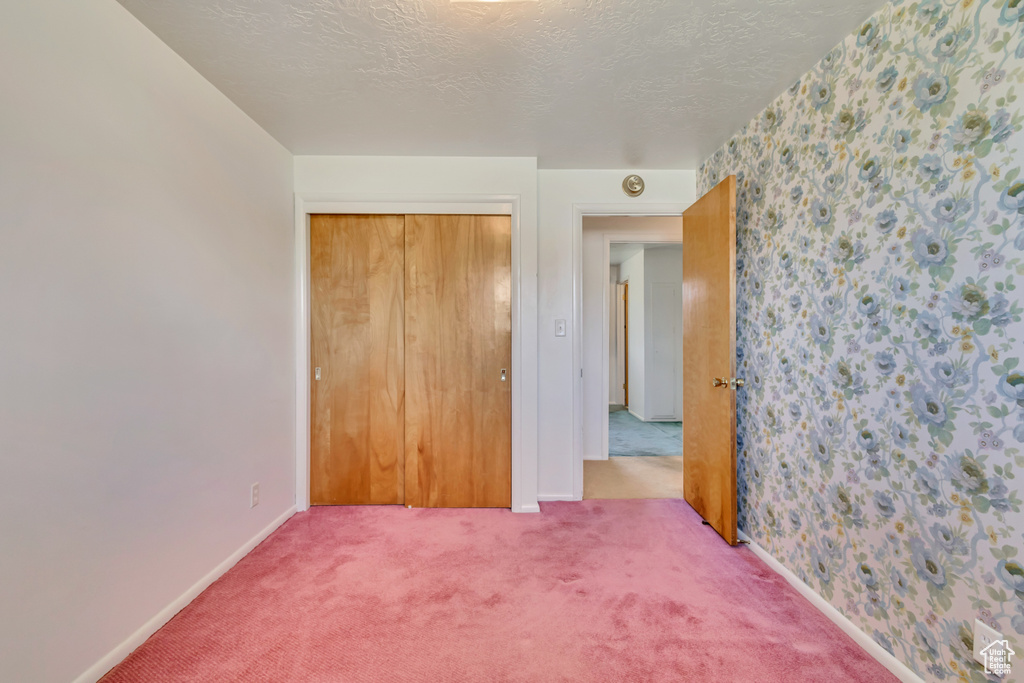 Unfurnished bedroom featuring a textured ceiling, carpet, baseboards, wallpapered walls, and a closet