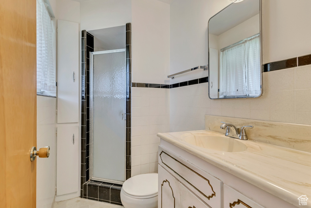 Full bath featuring vanity, a stall shower, toilet, and tile walls