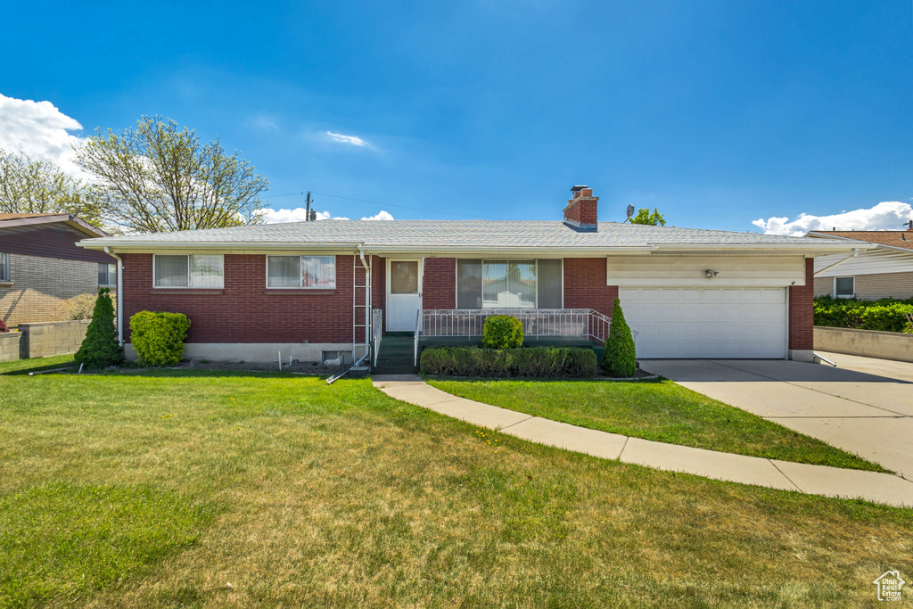 Single story home featuring an attached garage, a front lawn, brick siding, a chimney, and driveway
