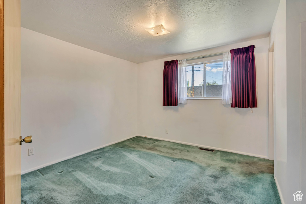Empty room with a textured ceiling, visible vents, baseboards, and carpet