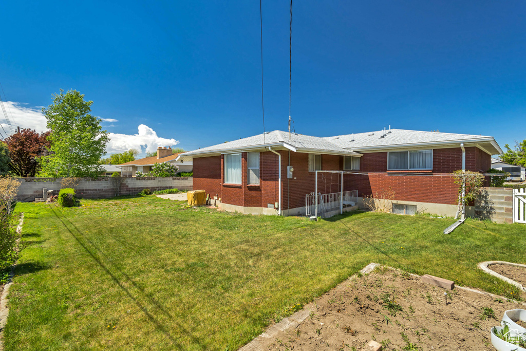 Back of property featuring a fenced backyard, a lawn, and brick siding