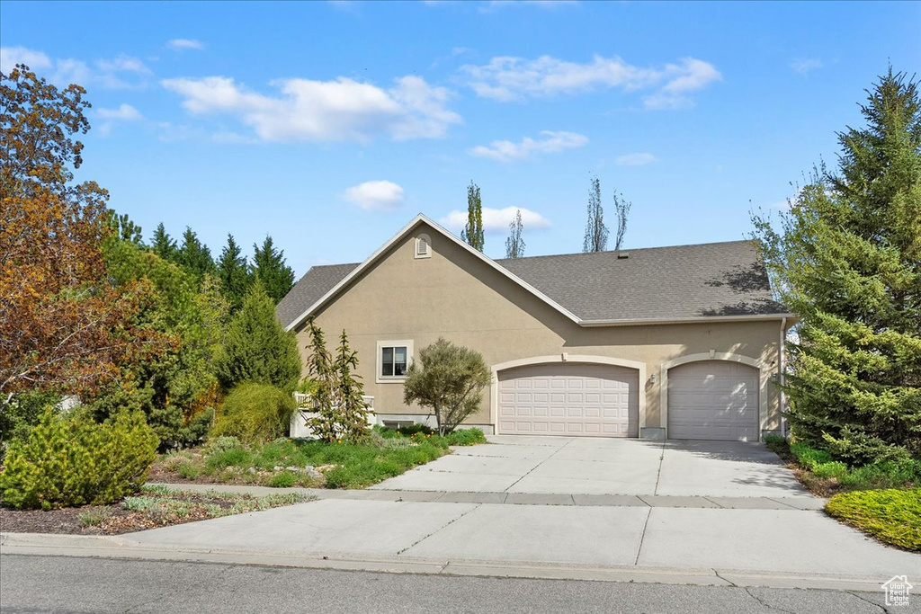 View of front facade featuring stucco siding, concrete driveway, a shingled roof, and a garage