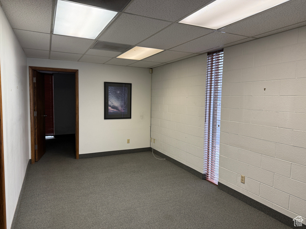 Spare room featuring dark colored carpet, a paneled ceiling, and baseboards