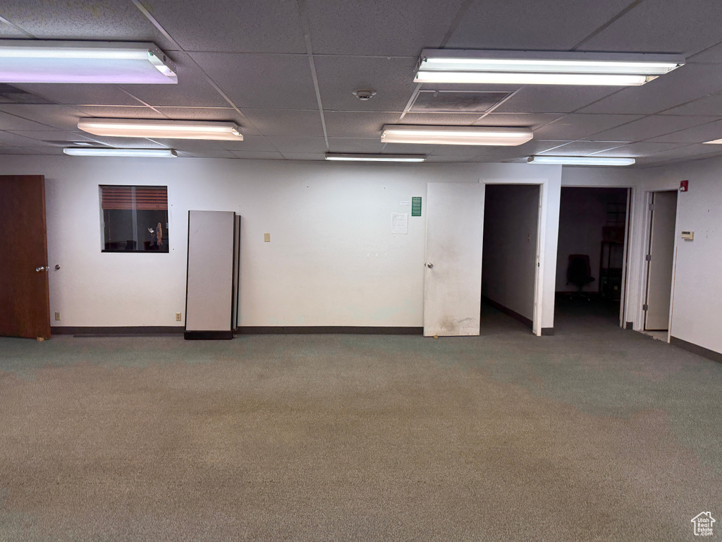 Carpeted spare room featuring baseboards and a drop ceiling
