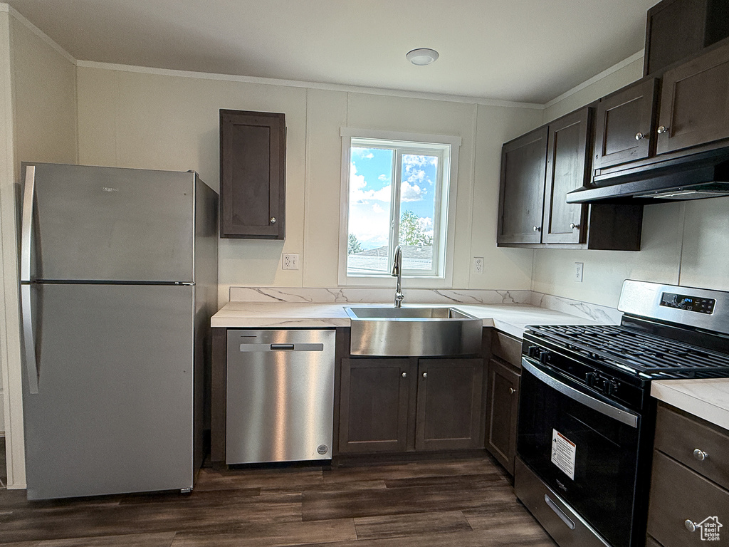 Kitchen with a sink, stainless steel appliances, under cabinet range hood, ornamental molding, and dark wood-type flooring