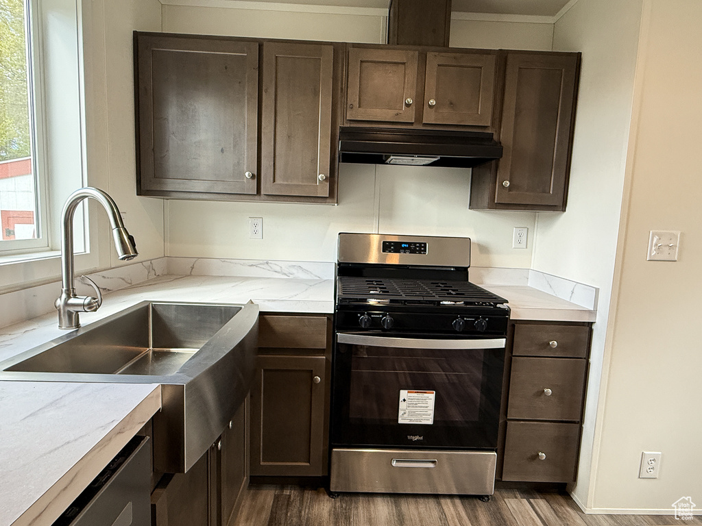 Kitchen with a sink, stainless steel range with gas stovetop, dark wood-style floors, and under cabinet range hood