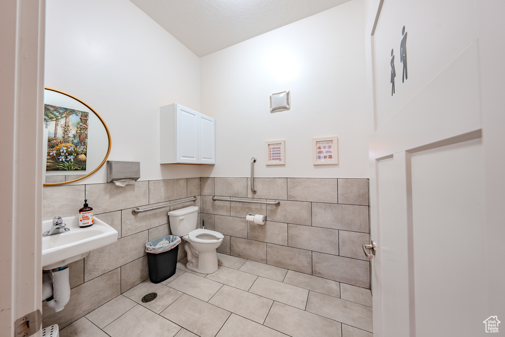Bathroom featuring tile walls, tile patterned flooring, vaulted ceiling, a wainscoted wall, and toilet